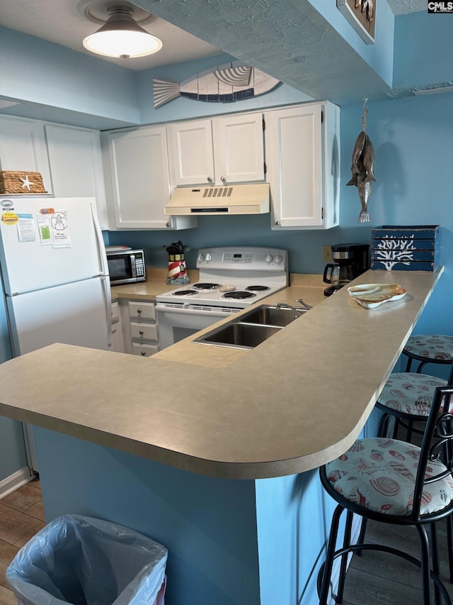 kitchen with kitchen peninsula, white appliances, hardwood / wood-style flooring, white cabinets, and a breakfast bar area