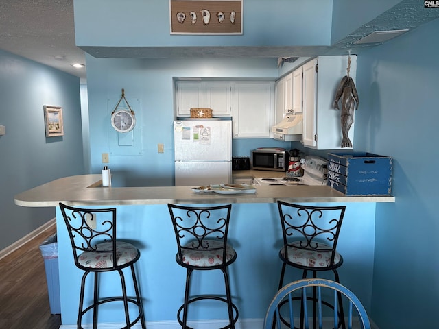 kitchen with white cabinets, a kitchen breakfast bar, range hood, fridge, and kitchen peninsula