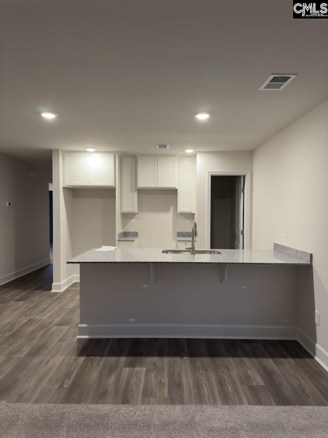 kitchen with sink, dark hardwood / wood-style flooring, white cabinetry, a kitchen bar, and kitchen peninsula