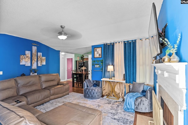 living room featuring a textured ceiling, vaulted ceiling, ceiling fan, and a premium fireplace