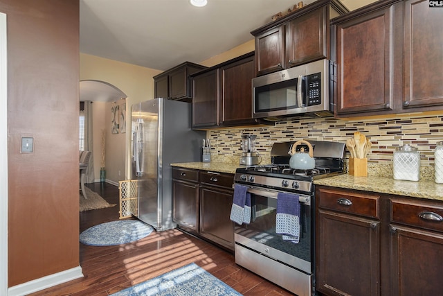 kitchen with appliances with stainless steel finishes, decorative backsplash, dark hardwood / wood-style floors, and light stone countertops