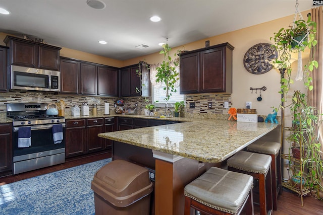 kitchen featuring light stone countertops, a kitchen bar, dark wood-type flooring, stainless steel appliances, and sink