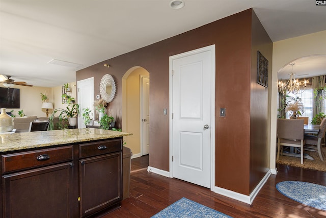 kitchen featuring light stone counters, ceiling fan with notable chandelier, dark hardwood / wood-style floors, and dark brown cabinetry