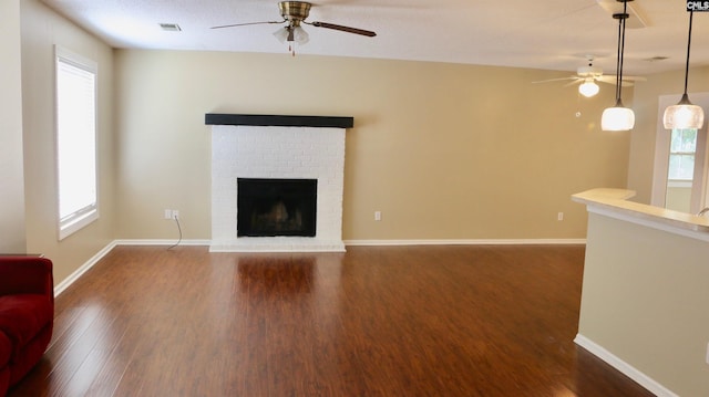 unfurnished living room with a wealth of natural light, ceiling fan, a fireplace, and wood finished floors