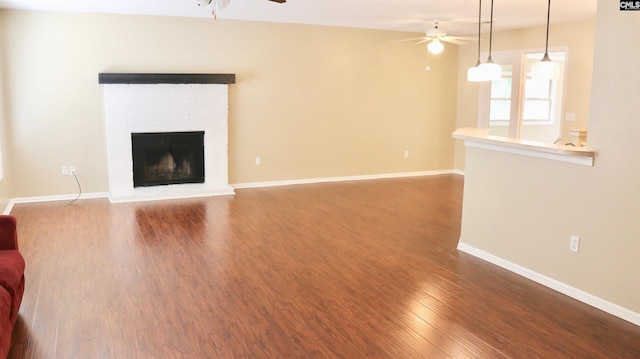 unfurnished living room with ceiling fan, a fireplace, baseboards, and dark wood-style flooring