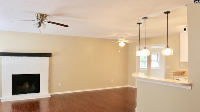 unfurnished living room featuring a brick fireplace, ceiling fan, baseboards, and dark wood-style flooring