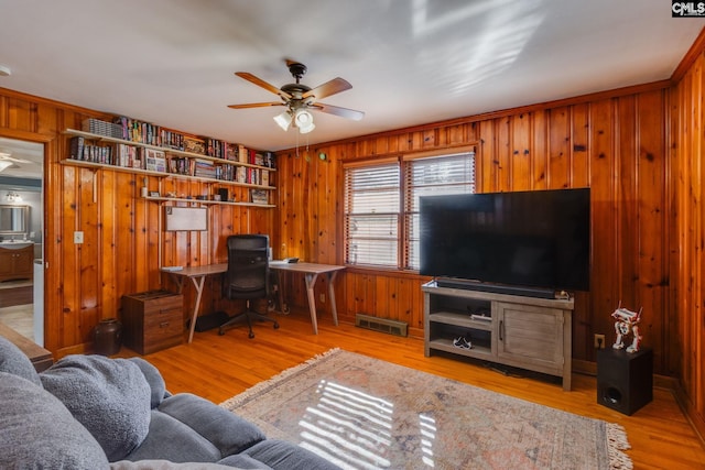 living room with ceiling fan, wooden walls, ornamental molding, and light wood-type flooring