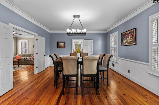 dining room with dark wood-type flooring, ornamental molding, and an inviting chandelier