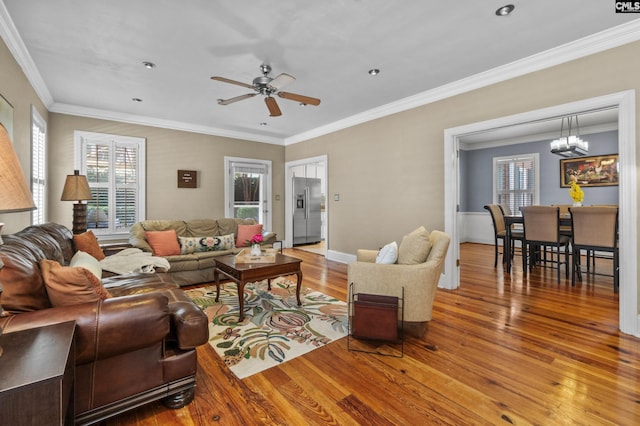 living room featuring hardwood / wood-style flooring, ornamental molding, and ceiling fan with notable chandelier