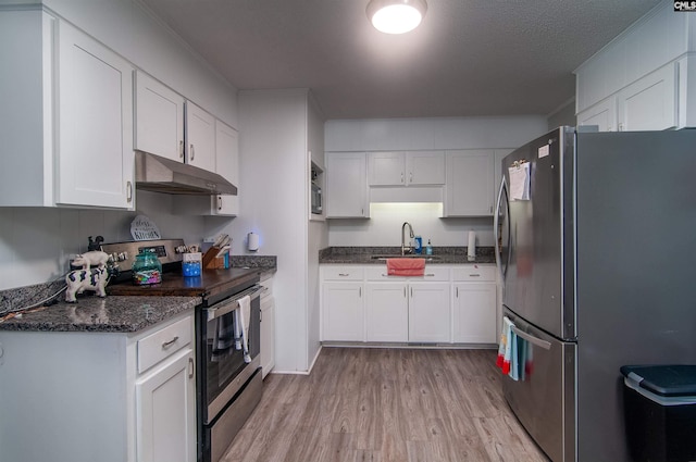 kitchen featuring appliances with stainless steel finishes, sink, dark stone countertops, light hardwood / wood-style floors, and white cabinetry