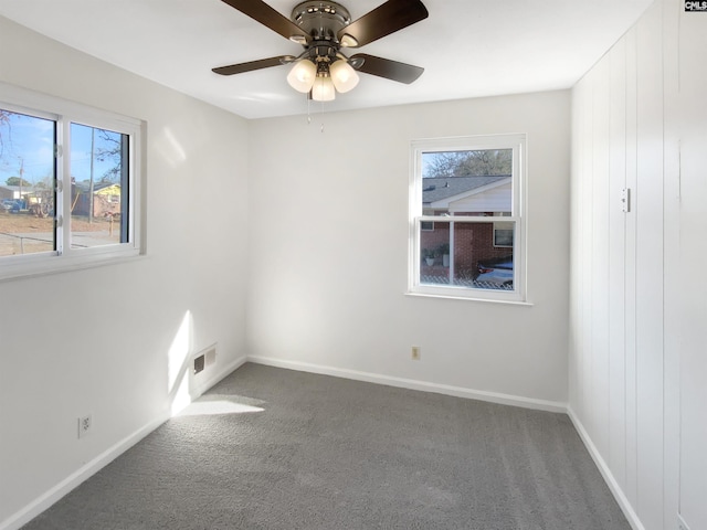 spare room featuring plenty of natural light, ceiling fan, and dark carpet