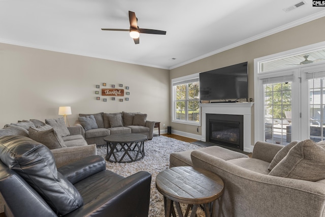 living room with wood-type flooring, a wealth of natural light, ornamental molding, and ceiling fan