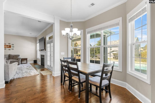 dining area with dark hardwood / wood-style floors, a healthy amount of sunlight, ornamental molding, and an inviting chandelier