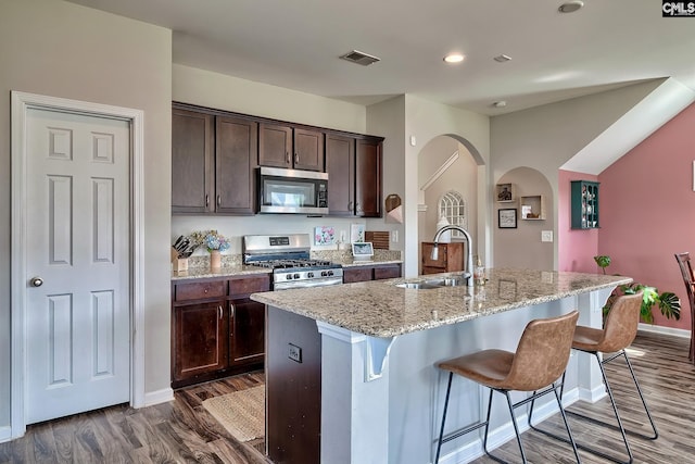 kitchen featuring a center island with sink, sink, appliances with stainless steel finishes, dark brown cabinets, and a breakfast bar area