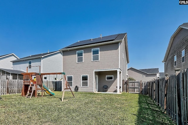 rear view of house featuring a lawn, solar panels, and a playground