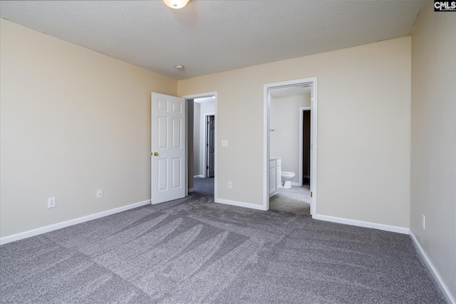 unfurnished bedroom featuring ensuite bath, a textured ceiling, and dark colored carpet