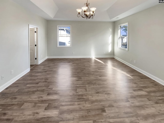 empty room featuring a tray ceiling, dark wood-type flooring, a healthy amount of sunlight, and a notable chandelier