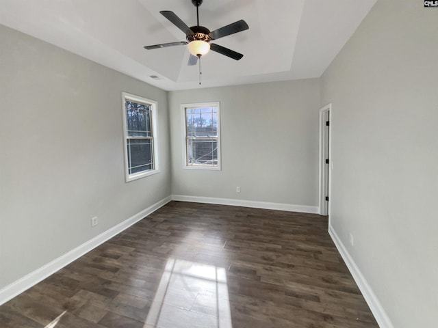 spare room with a raised ceiling, ceiling fan, and dark hardwood / wood-style flooring