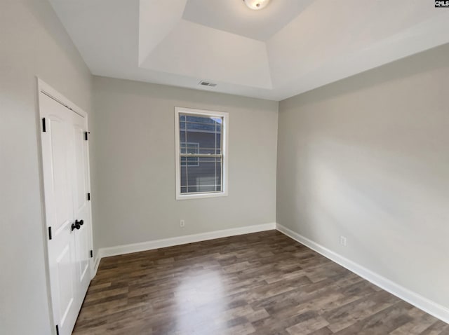 spare room featuring a raised ceiling and dark wood-type flooring