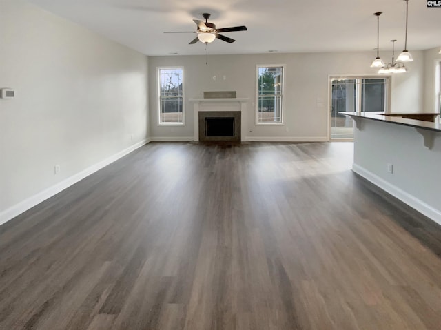 unfurnished living room with a fireplace, ceiling fan with notable chandelier, and dark hardwood / wood-style floors