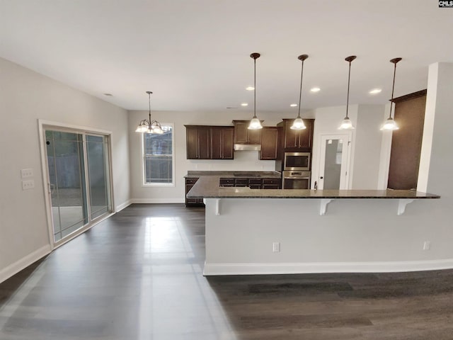 kitchen with an inviting chandelier, a kitchen breakfast bar, dark stone countertops, decorative light fixtures, and dark brown cabinetry