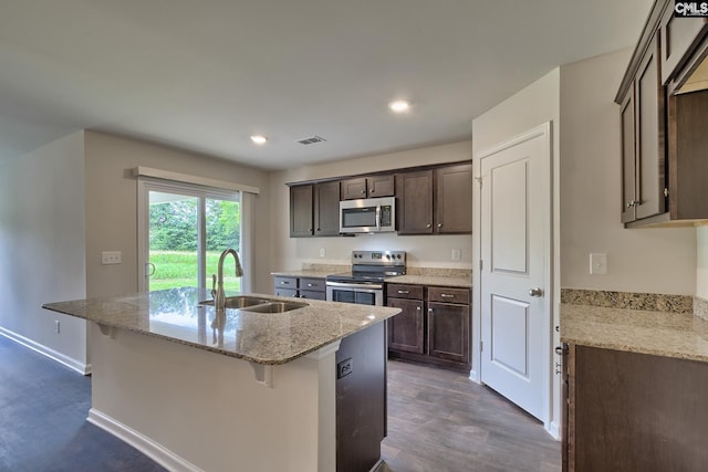 kitchen featuring sink, a breakfast bar area, appliances with stainless steel finishes, light stone countertops, and a kitchen island with sink