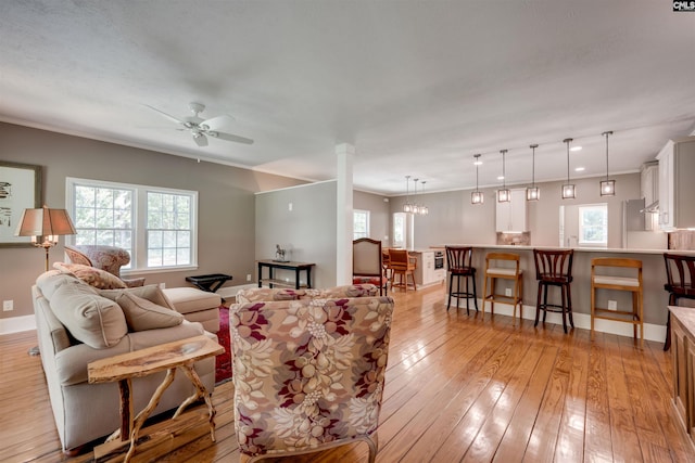 living room featuring light wood-type flooring, ceiling fan with notable chandelier, and ornamental molding