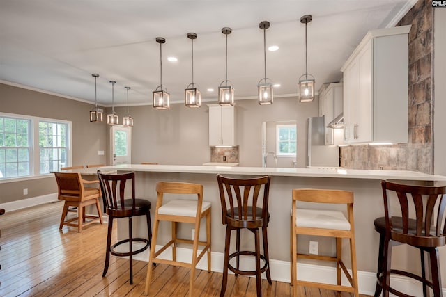 kitchen with white cabinetry, tasteful backsplash, pendant lighting, a kitchen bar, and light wood-type flooring