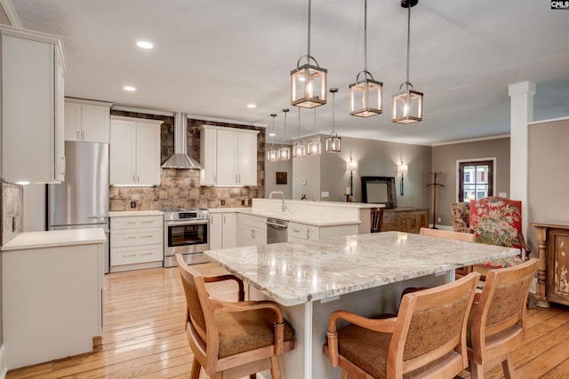 kitchen with kitchen peninsula, appliances with stainless steel finishes, wall chimney exhaust hood, hanging light fixtures, and a breakfast bar area