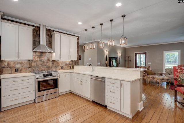 kitchen with wall chimney exhaust hood, hanging light fixtures, stainless steel appliances, kitchen peninsula, and crown molding