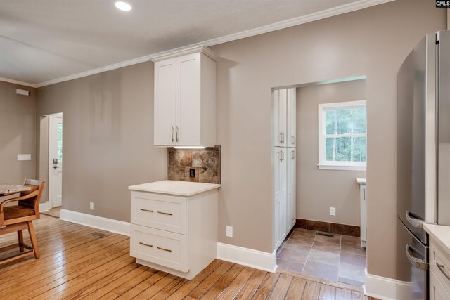 kitchen with white cabinets, light wood-type flooring, stainless steel refrigerator, and crown molding