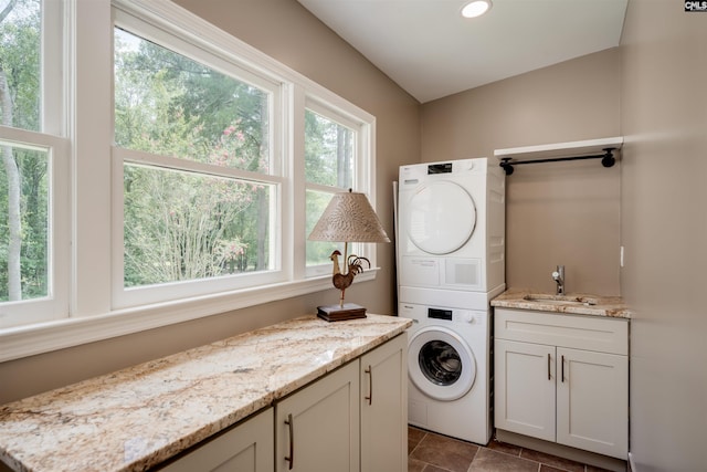 washroom with cabinets, stacked washer and dryer, and sink