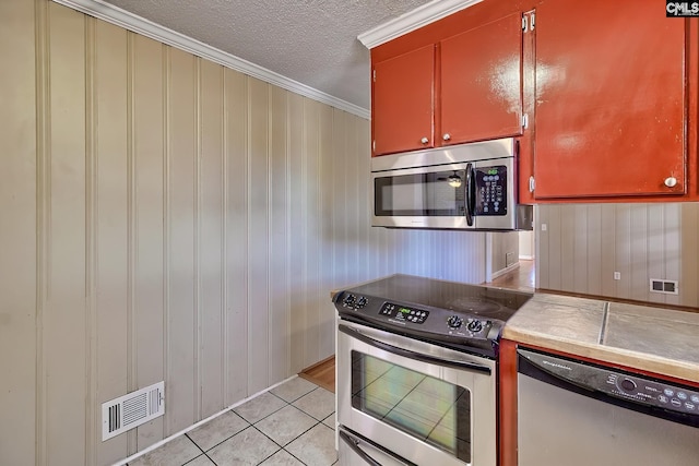 kitchen with wood walls, crown molding, a textured ceiling, appliances with stainless steel finishes, and light tile patterned flooring