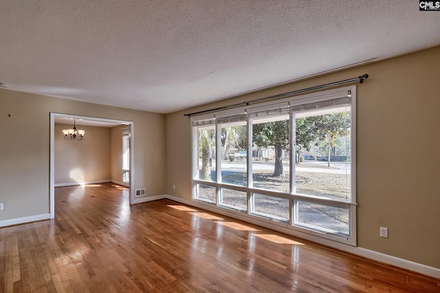 empty room with a chandelier, hardwood / wood-style floors, and plenty of natural light