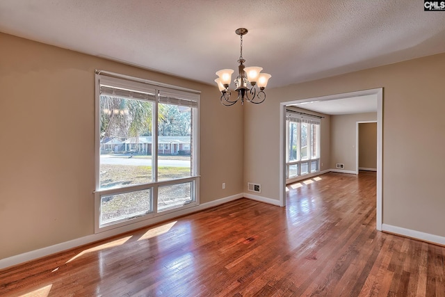 spare room with a chandelier, hardwood / wood-style floors, and a textured ceiling