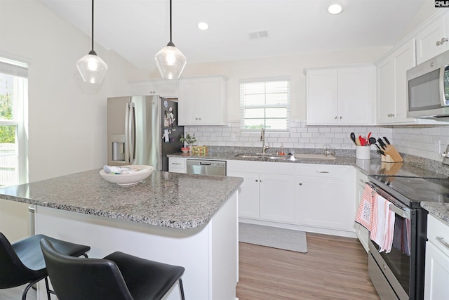 kitchen featuring decorative light fixtures, a kitchen island, white cabinetry, and stainless steel appliances