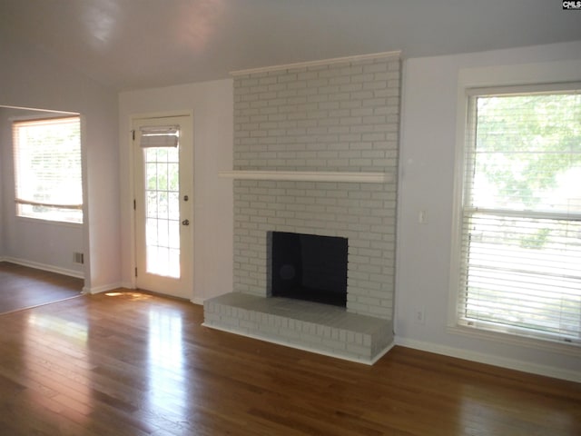 unfurnished living room featuring vaulted ceiling, a brick fireplace, and dark wood-type flooring