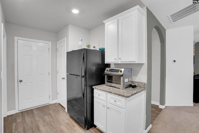 kitchen with arched walkways, visible vents, light wood-style floors, freestanding refrigerator, and light stone countertops