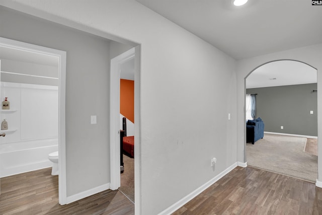 corridor with arched walkways, baseboards, and wood finished floors