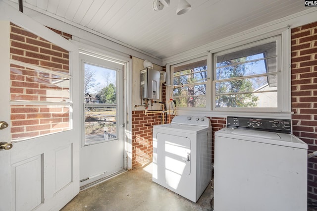 clothes washing area with washer and dryer, brick wall, and water heater