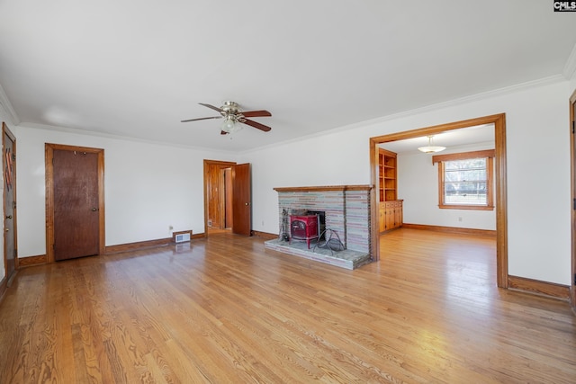 unfurnished living room featuring ceiling fan, ornamental molding, a wood stove, and light hardwood / wood-style flooring