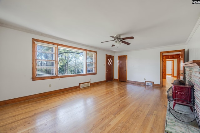 unfurnished living room with ceiling fan, a wood stove, crown molding, and light hardwood / wood-style flooring