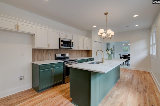 kitchen with stainless steel appliances, sink, pendant lighting, white cabinetry, and an island with sink