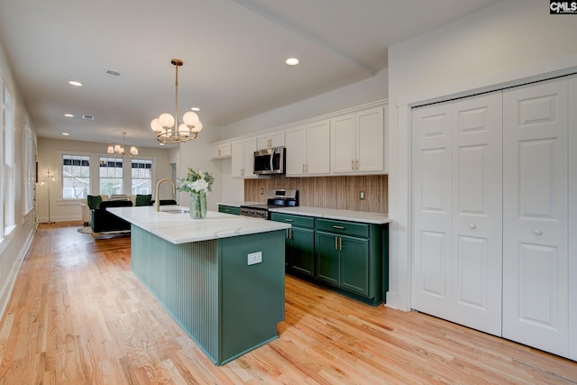 kitchen featuring a kitchen island with sink, white cabinets, decorative light fixtures, a notable chandelier, and stainless steel appliances