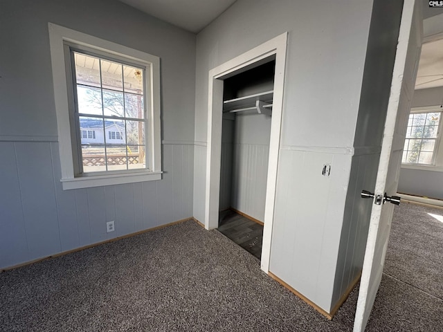 unfurnished bedroom with dark colored carpet, multiple windows, and a closet