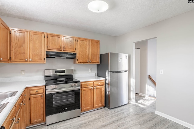 kitchen with appliances with stainless steel finishes, a textured ceiling, and light hardwood / wood-style flooring