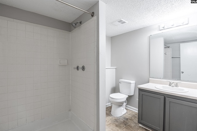 bathroom featuring vanity, toilet, a textured ceiling, and a tile shower