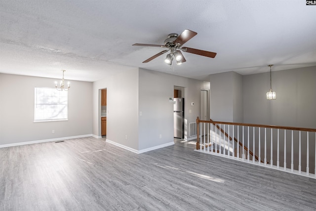 unfurnished room with ceiling fan with notable chandelier, wood-type flooring, and a textured ceiling