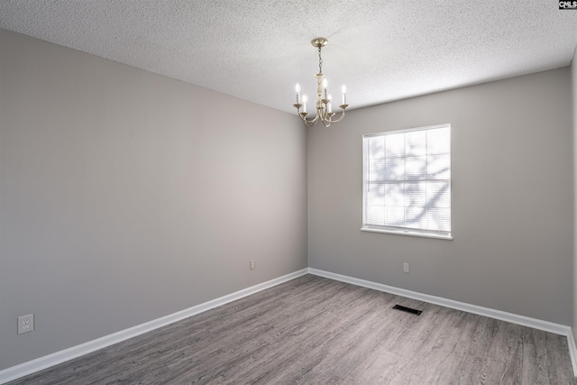 empty room featuring hardwood / wood-style floors, a textured ceiling, and an inviting chandelier