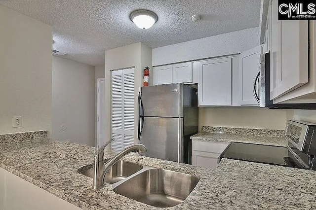 kitchen with white cabinetry, sink, light stone countertops, a textured ceiling, and appliances with stainless steel finishes